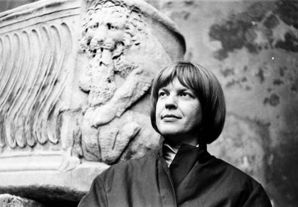 Woman with short hair in a dark coat standing beside a carved stone lion sculpture, looking upward thoughtfully (black and white photo).