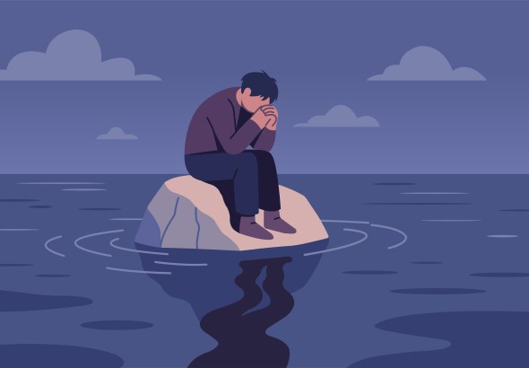 A person sits on a rock by the water, head in hands, appearing sad or distressed at dusk.