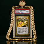 Gold-plated pendant necklace featuring a framed Pikachu Illustrator card on a dark background with a diamond-studded chain.